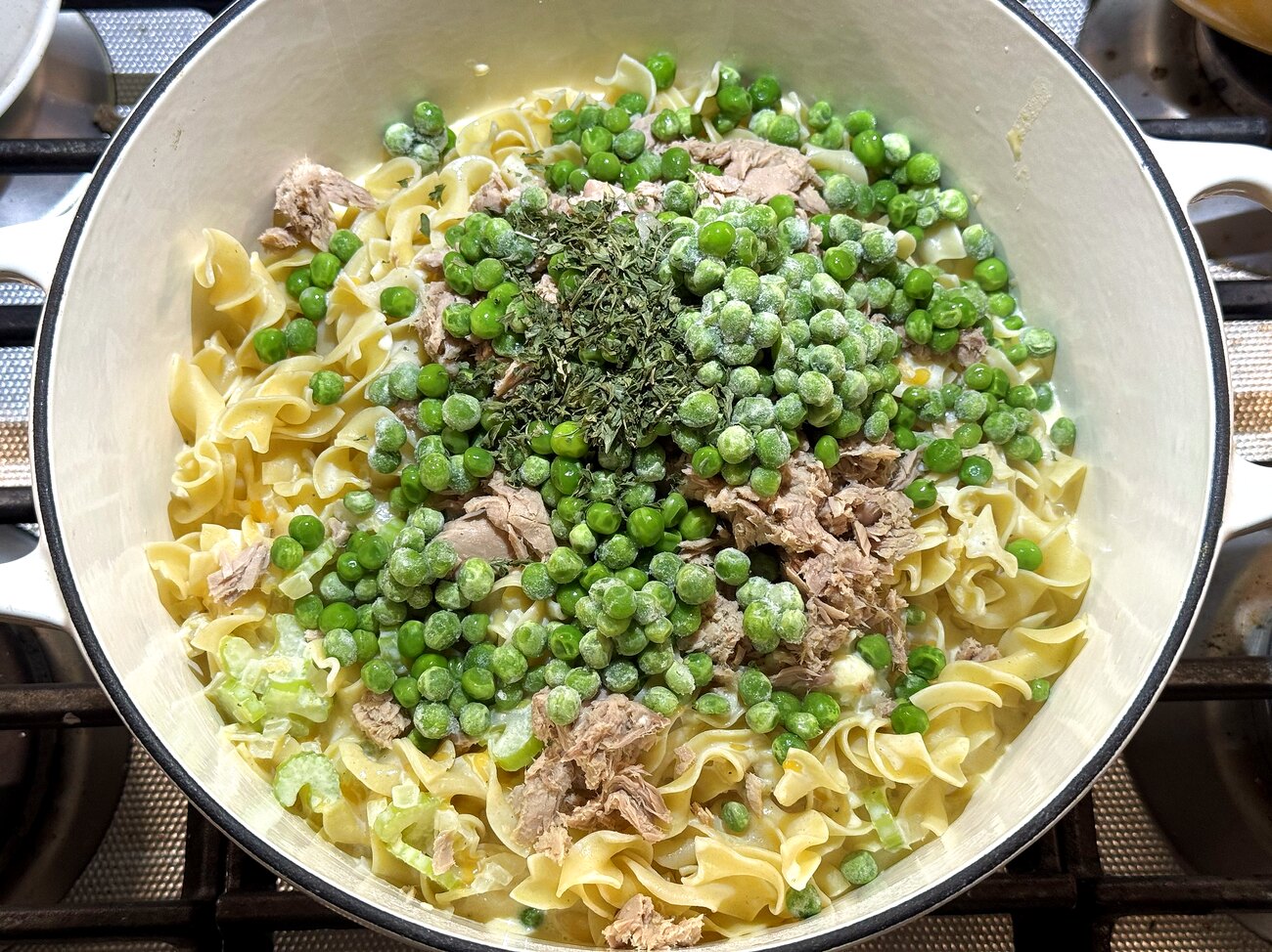 Egg noodles, flaked tuna, peas, and parsley added to the creamy sauce in the pot