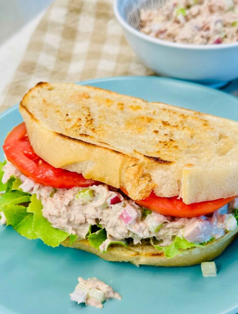 Tuna salad sandwich on toasted sourdough with lettuce and tomato on a blue plate