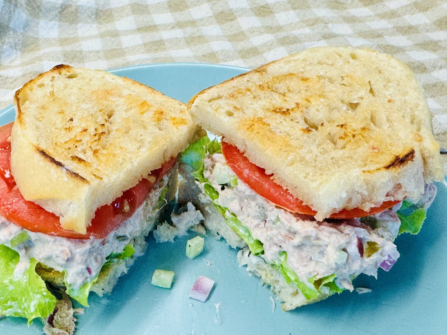 Tuna salad sandwich on toasted sourdough cut in half on a blue plate