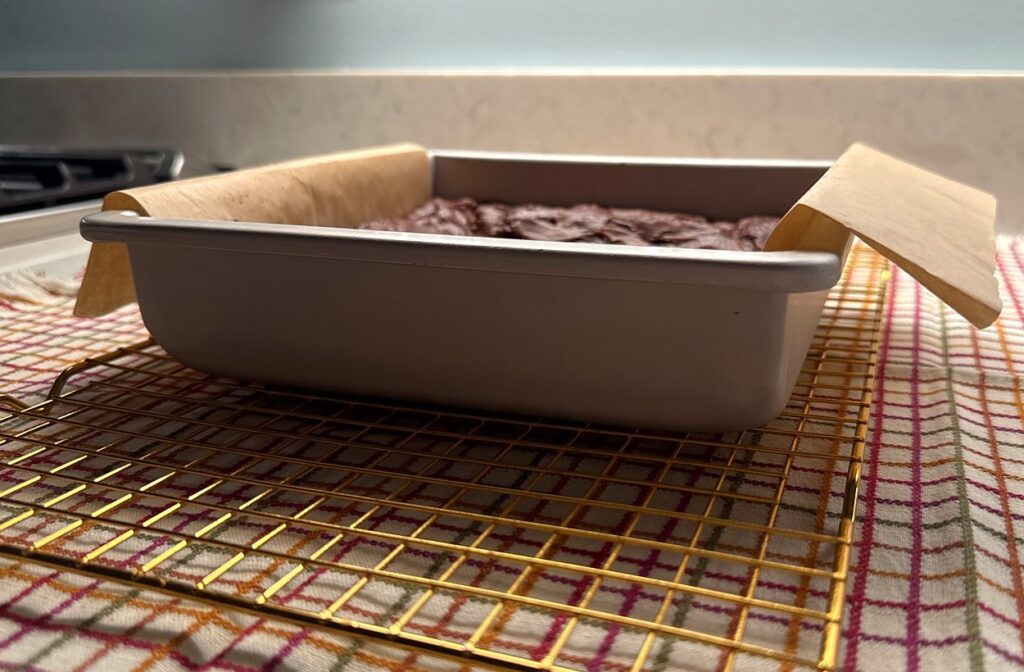 A pan of brownies cooling on a gold wire rack on the kitchen counter