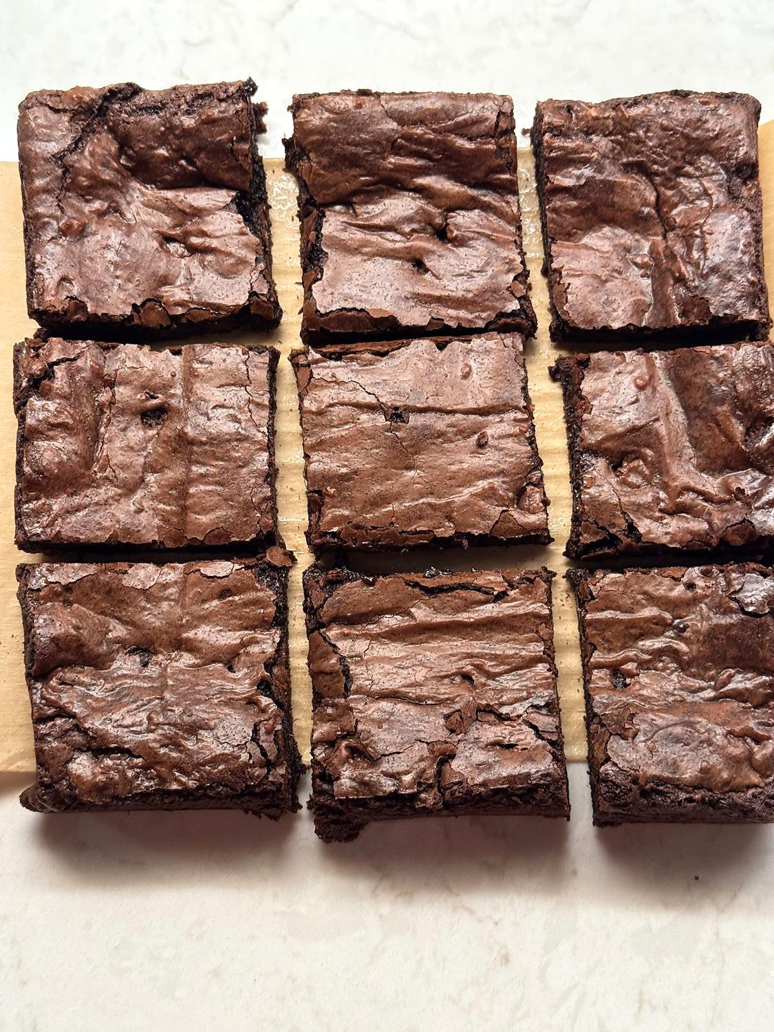 Nine homemade brownie squares cut and slightly separated on parchment paper