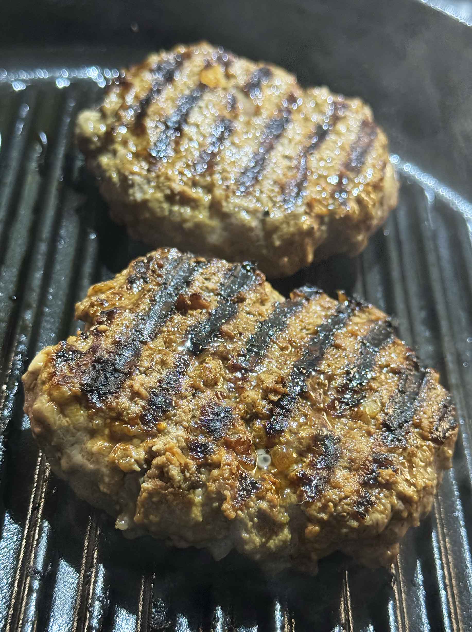 Two burger patties searing in a cast iron grill pan with dark grill marks