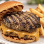 Two homemade burger patties and a slice of cheese on a bun with a side of fries
