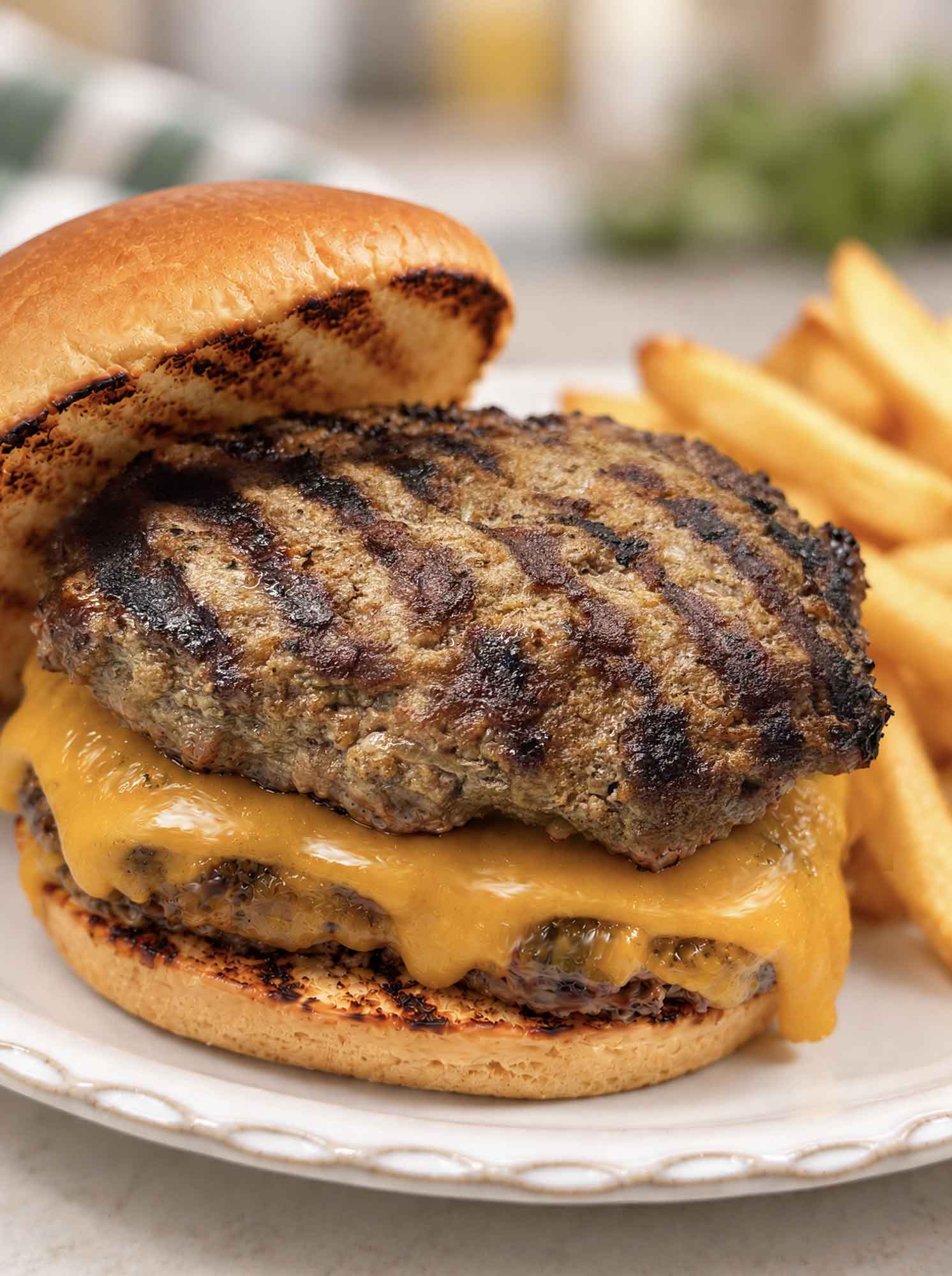 Two homemade burger patties and a slice of cheese on a bun with a side of fries