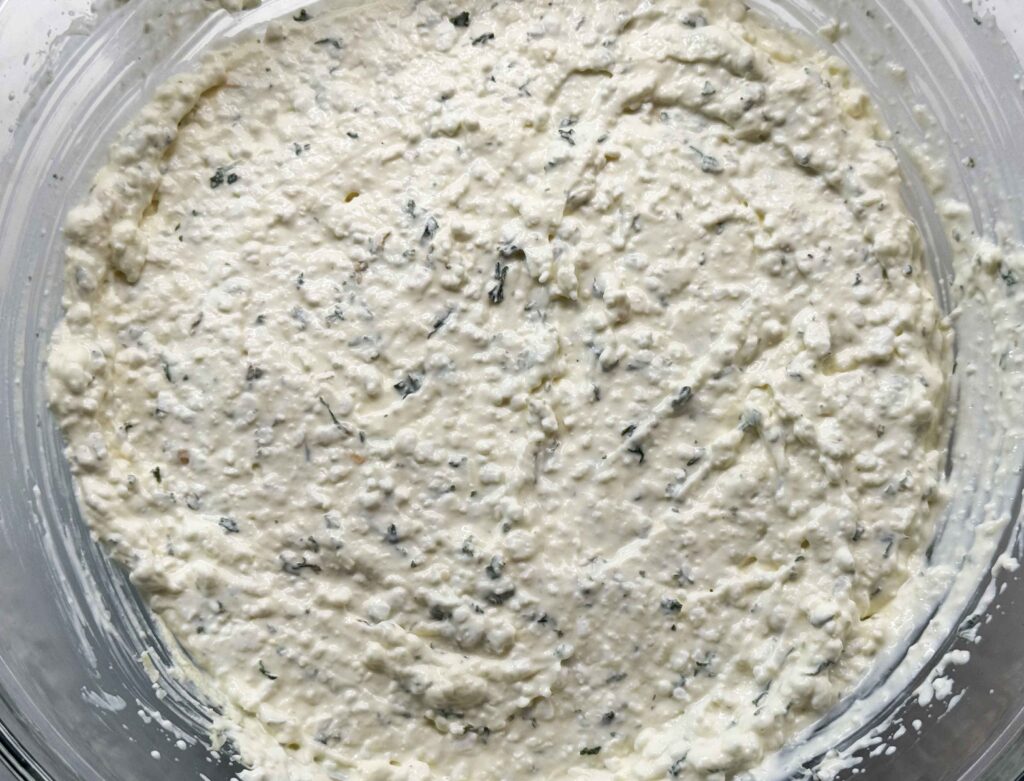 The finished cottage cheese and cream cheese mixture in a glass bowl, thick and flecked with parsley and Parmesan.