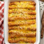 Easy chicken enchiladas in a white baking dish, covered in melted cheese and red enchilada sauce and sprinkled with fresh chives