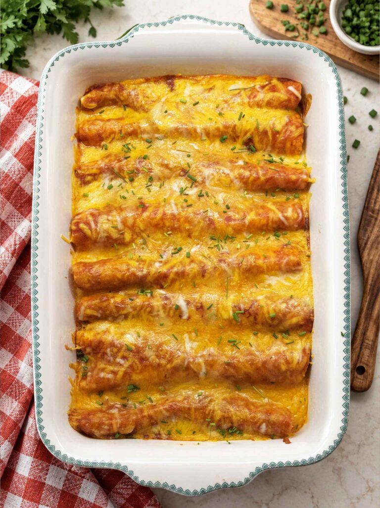 Easy chicken enchiladas in a white baking dish, covered in melted cheese and red enchilada sauce and sprinkled with fresh chives