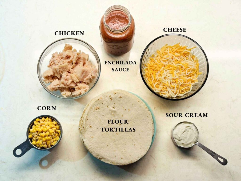 Labeled ingredients for easy chicken enchiladas: canned chicken, red enchilada sauce, shredded cheese, flour tortillas, corn, and sour cream