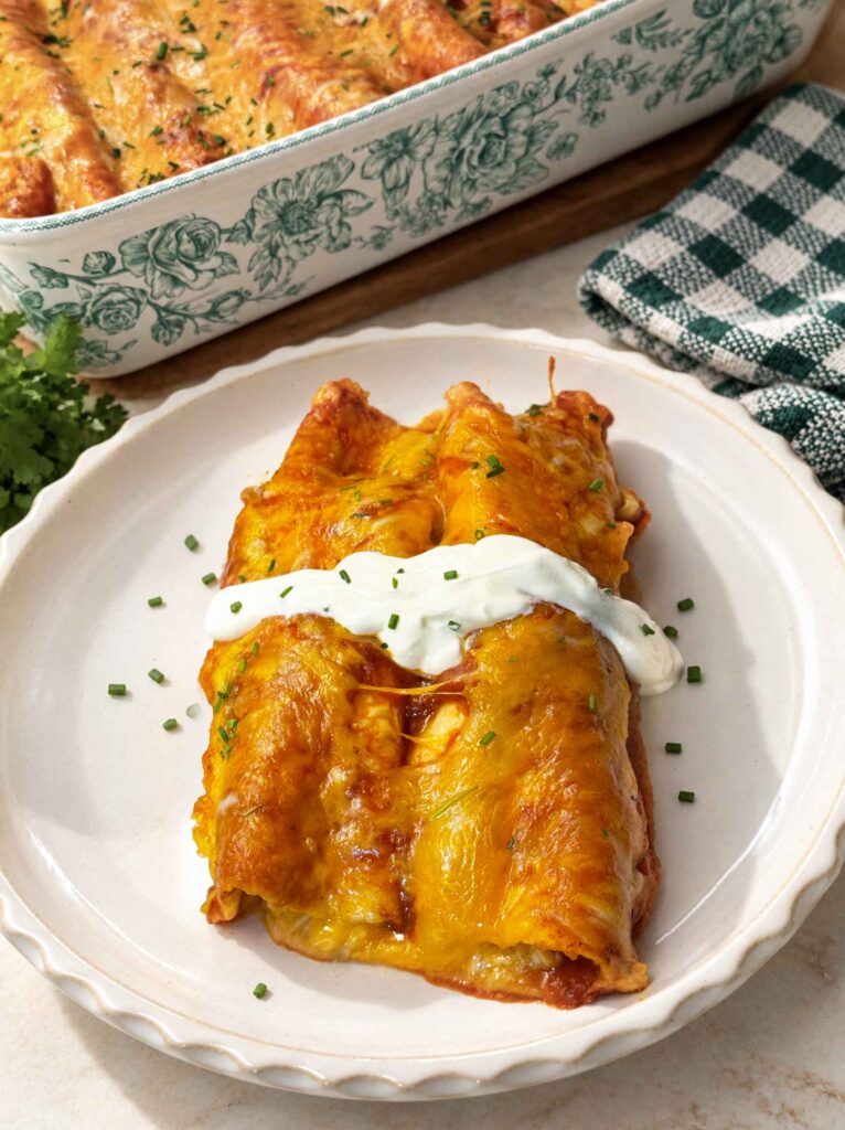 Two chicken enchiladas on a white plate topped with a stripe of sour cream and chopped chives