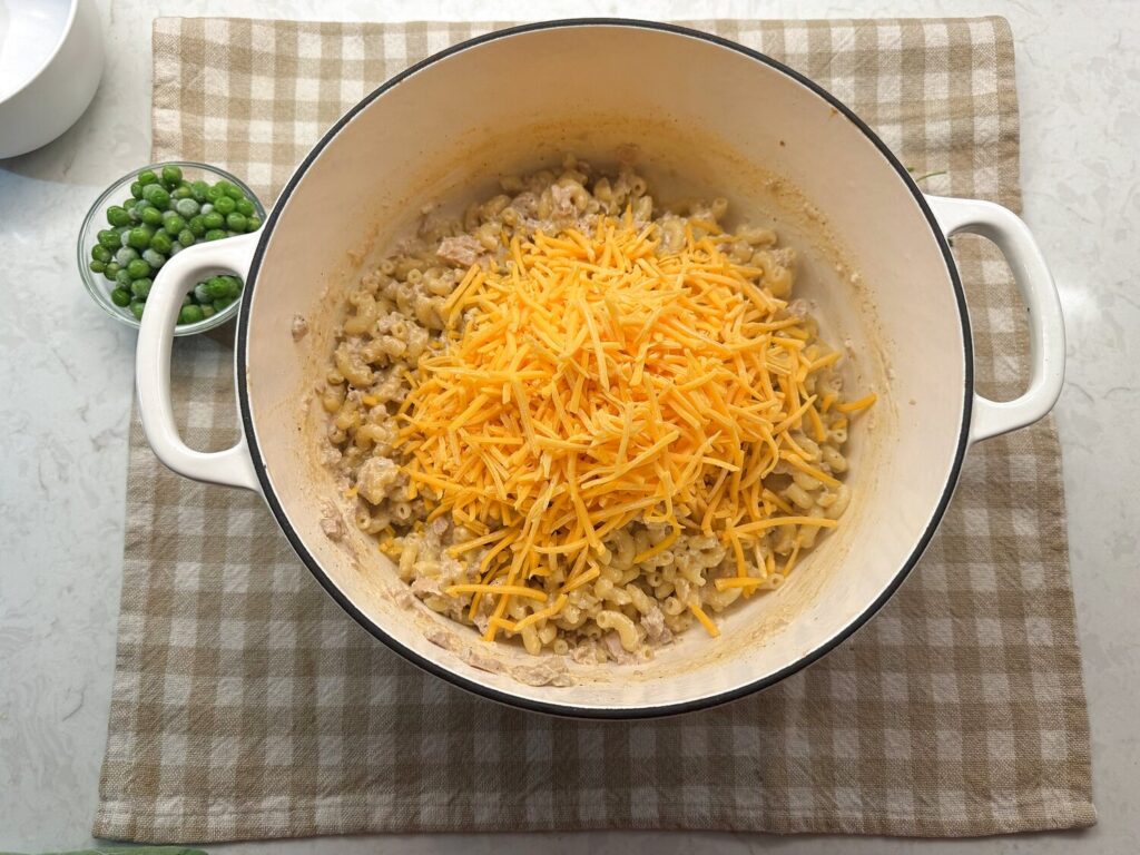 A pile of shredded cheddar cheese on top of the cooked tuna macaroni in the Dutch oven