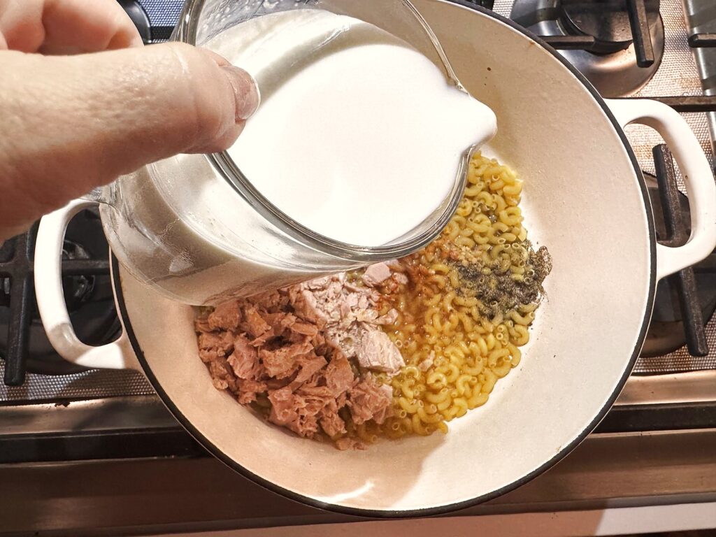 Pouring milk into the pot to make creamy tuna pasta