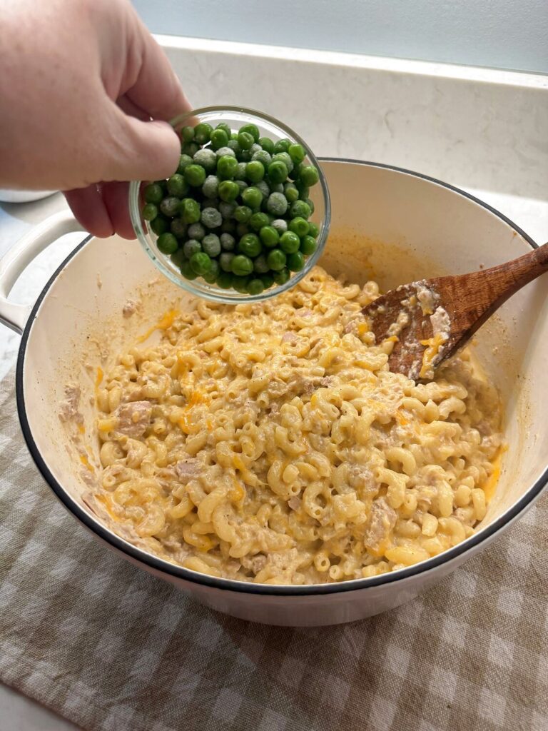 Frozen peas being tipped from a glass bowl into the cheesy tuna macaroni
