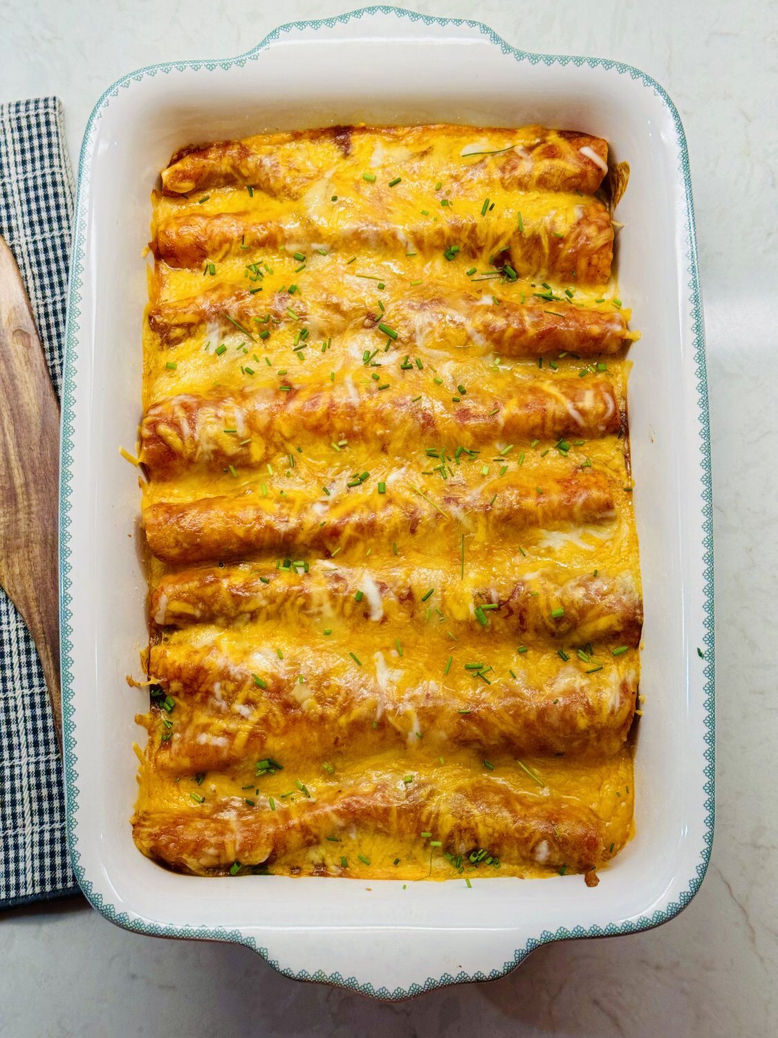 Baked chicken enchiladas in a white dish with bubbling melted cheese and chopped chives
