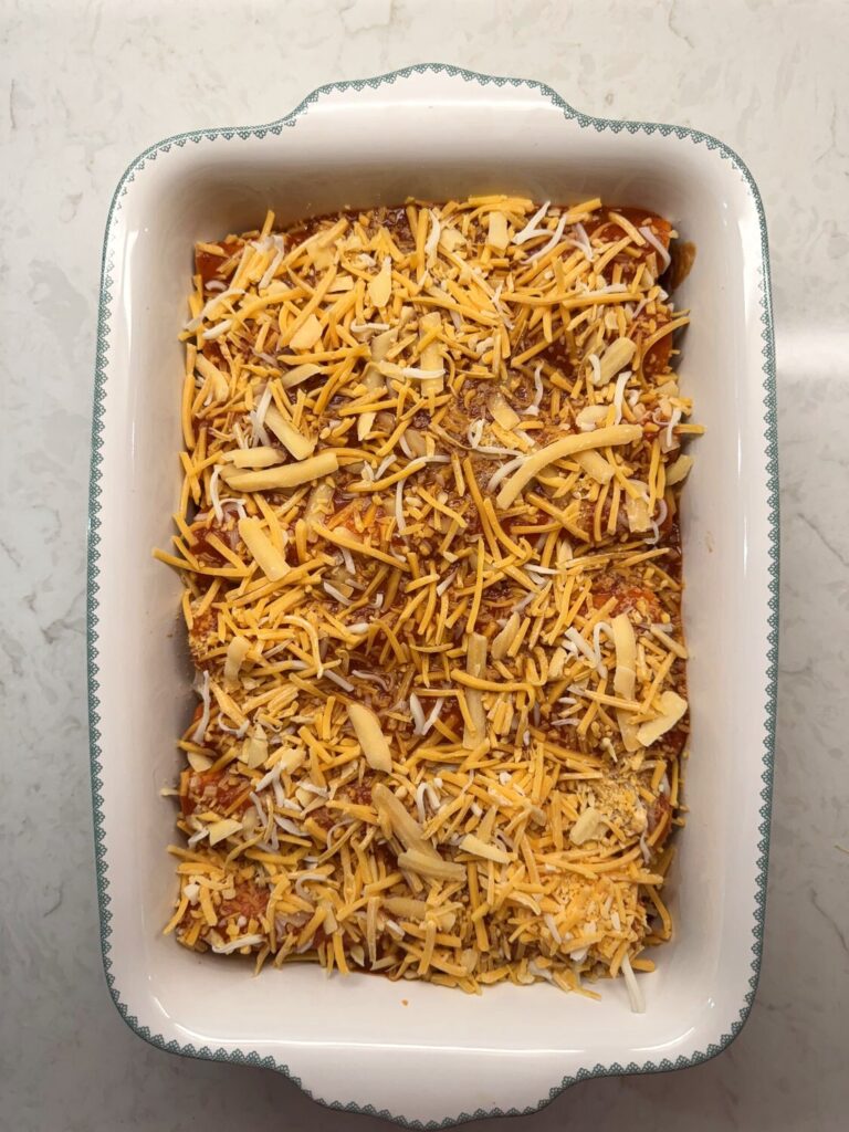 Shredded cheese sprinkled over sauced enchiladas before baking