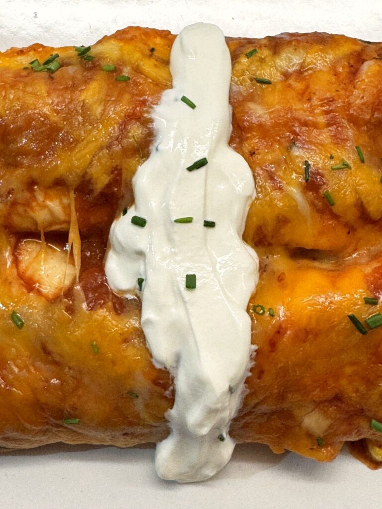 Close-up of a cheesy chicken enchilada topped with sour cream and chives
