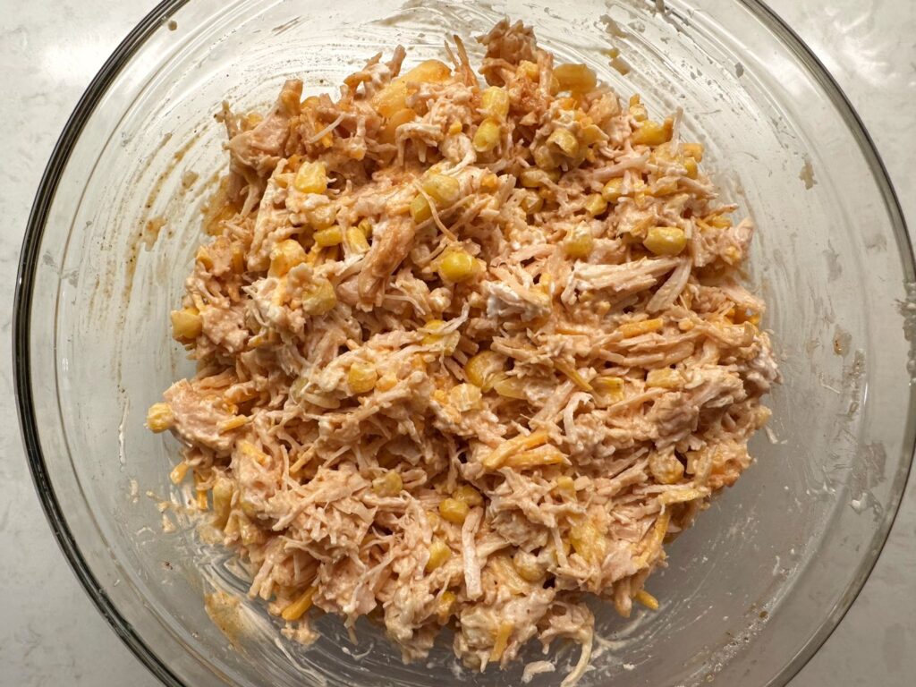 Creamy chicken enchilada filling with corn and shredded cheese mixed in a glass bowl