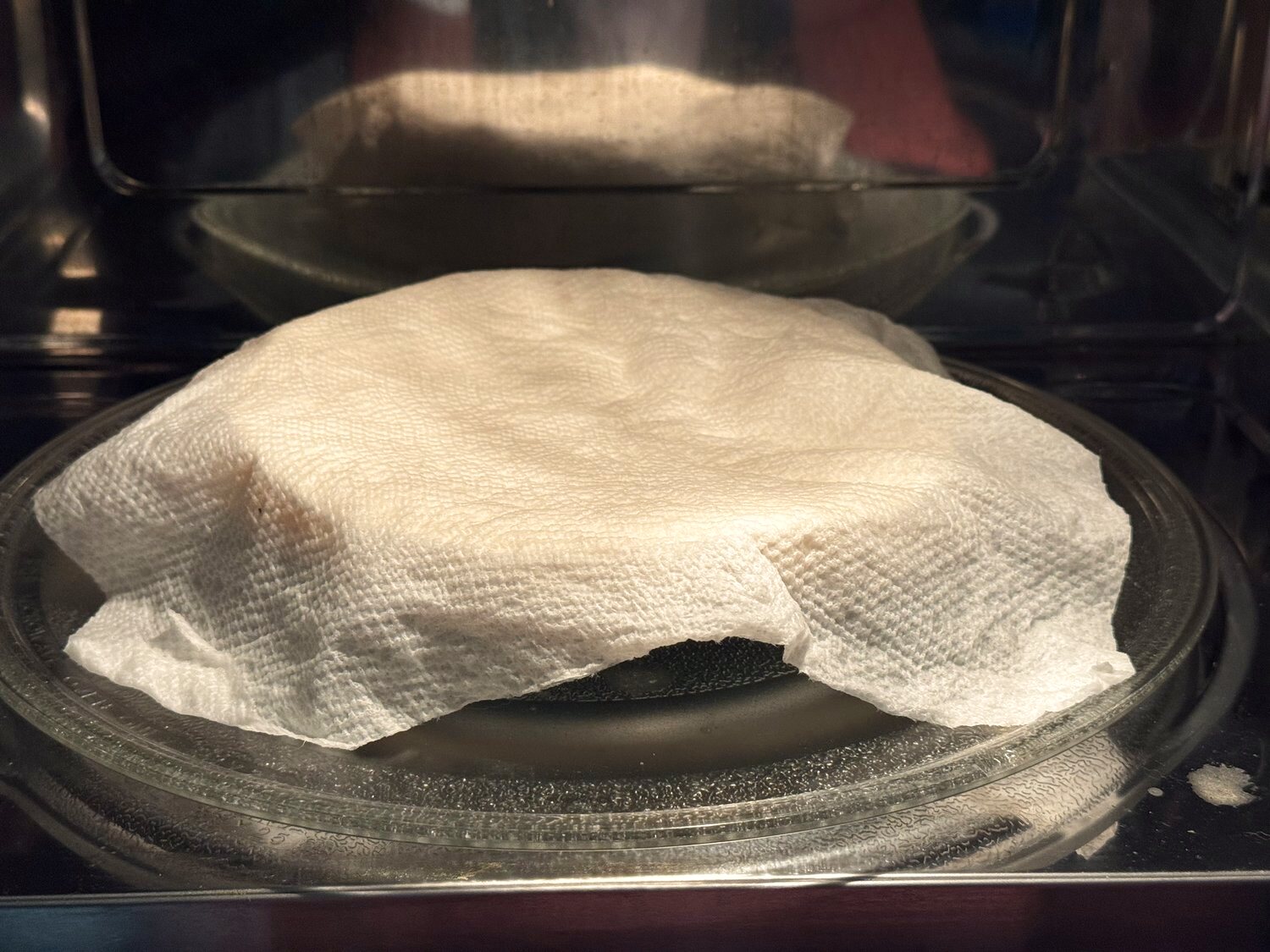 A stack of flour tortillas covered with a damp paper towel in the microwave