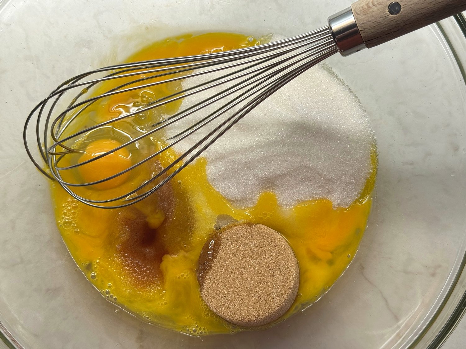 Two eggs, granulated sugar, packed brown sugar, and vanilla in a large glass mixing bowl with a whisk