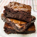 A stack of three fudgy homemade brownies with shiny crackly tops on a white plate