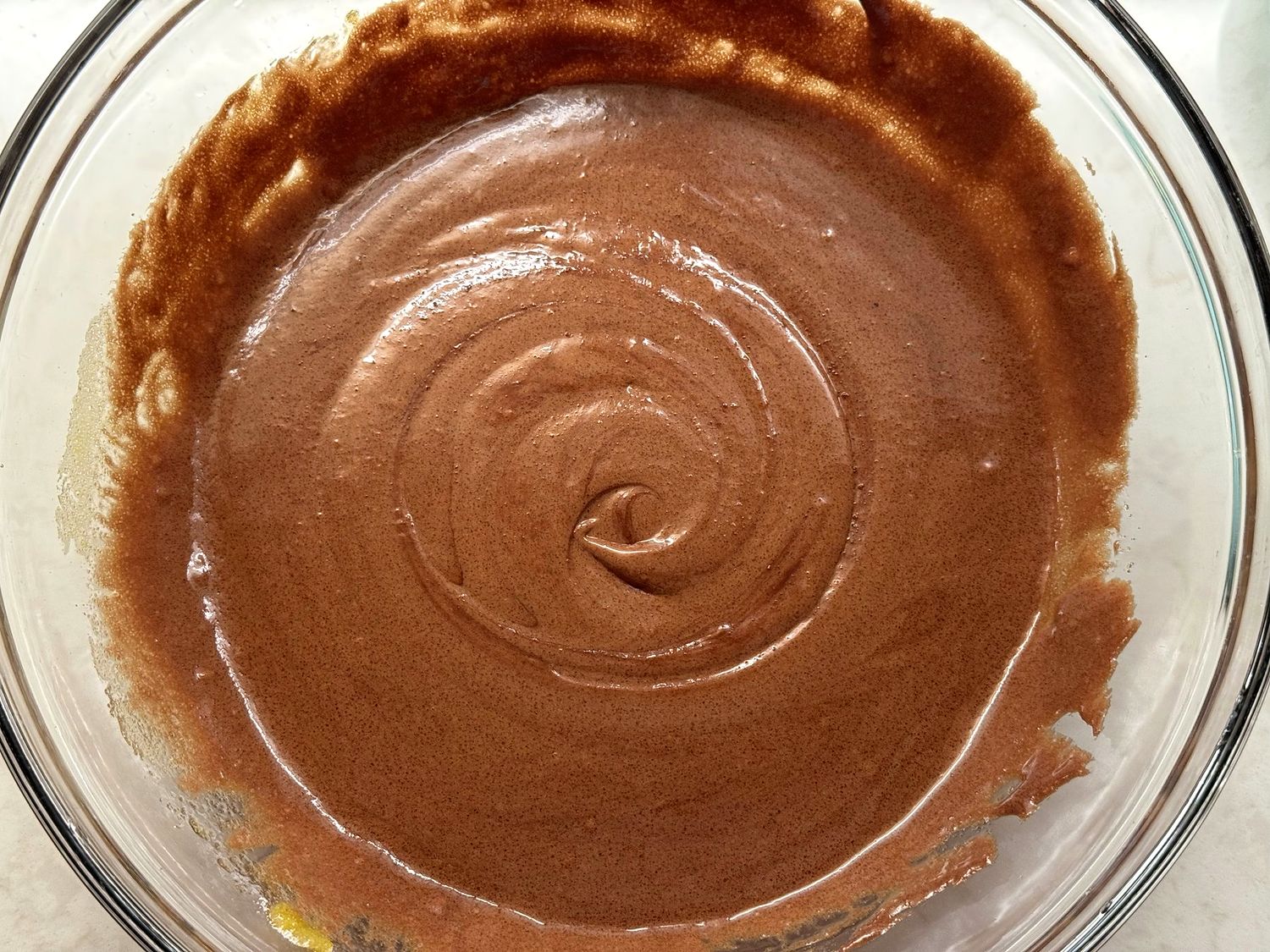 Smooth, glossy chocolate brownie batter swirled in a glass bowl