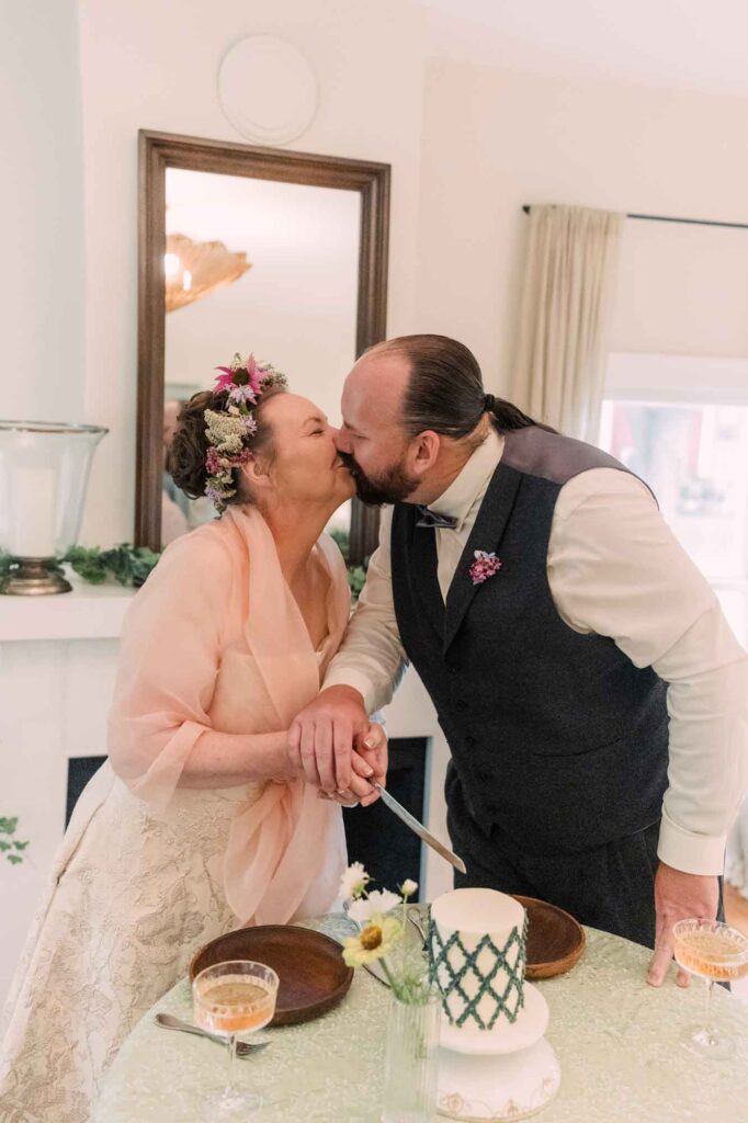 Jennifer and Greg kiss while cutting their wedding cake