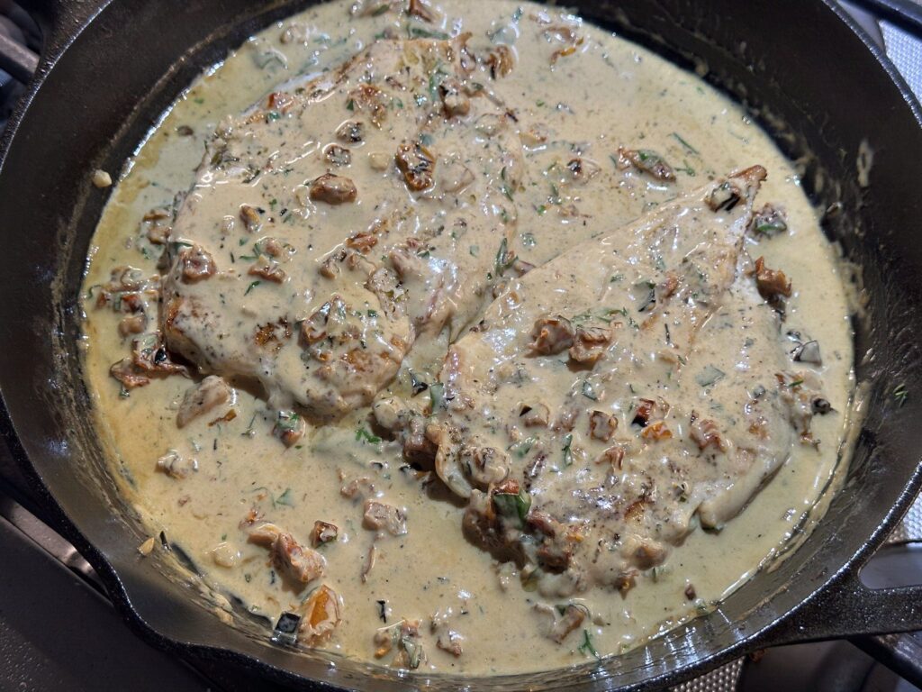 Creamy Parmesan and sun-dried tomato sauce with chicken simmering in the skillet