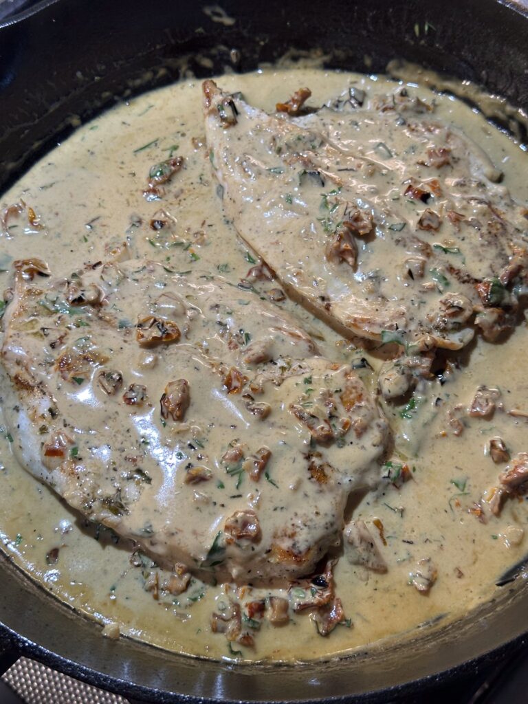 Finished He Married Me Chicken resting in creamy sun-dried tomato sauce in a cast iron skillet