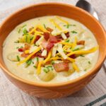 A bowl of loaded potato soup topped with crispy bacon, shredded yellow and white cheddar cheese, and fresh chives