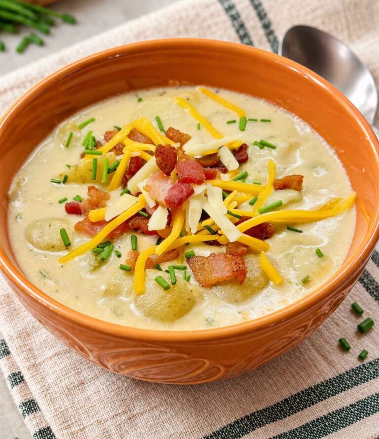A bowl of loaded potato soup topped with crispy bacon, shredded yellow and white cheddar cheese, and fresh chives