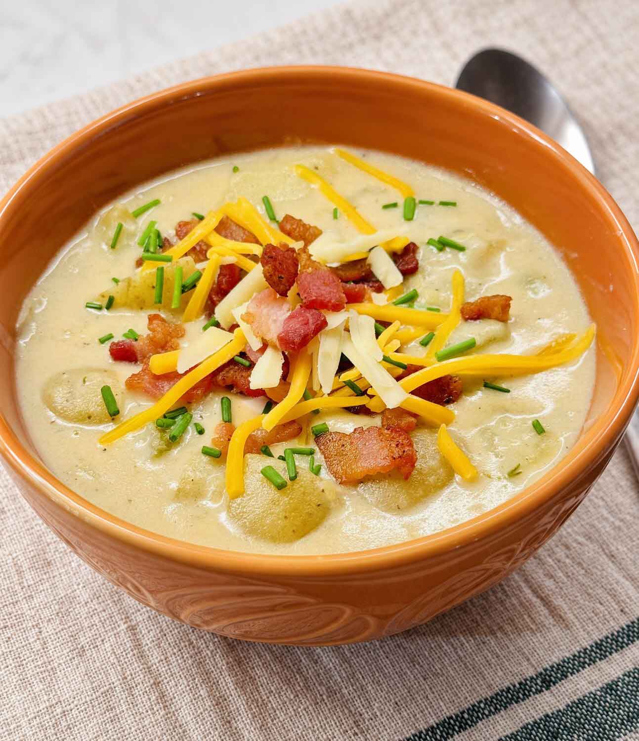 A bowl of loaded potato soup topped with crispy bacon, shredded yellow and white cheddar cheese, and fresh chives