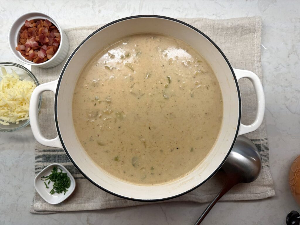 Overhead view of a bowl of loaded potato soup with bacon, cheddar, and chives on a striped linen towel with a spoon