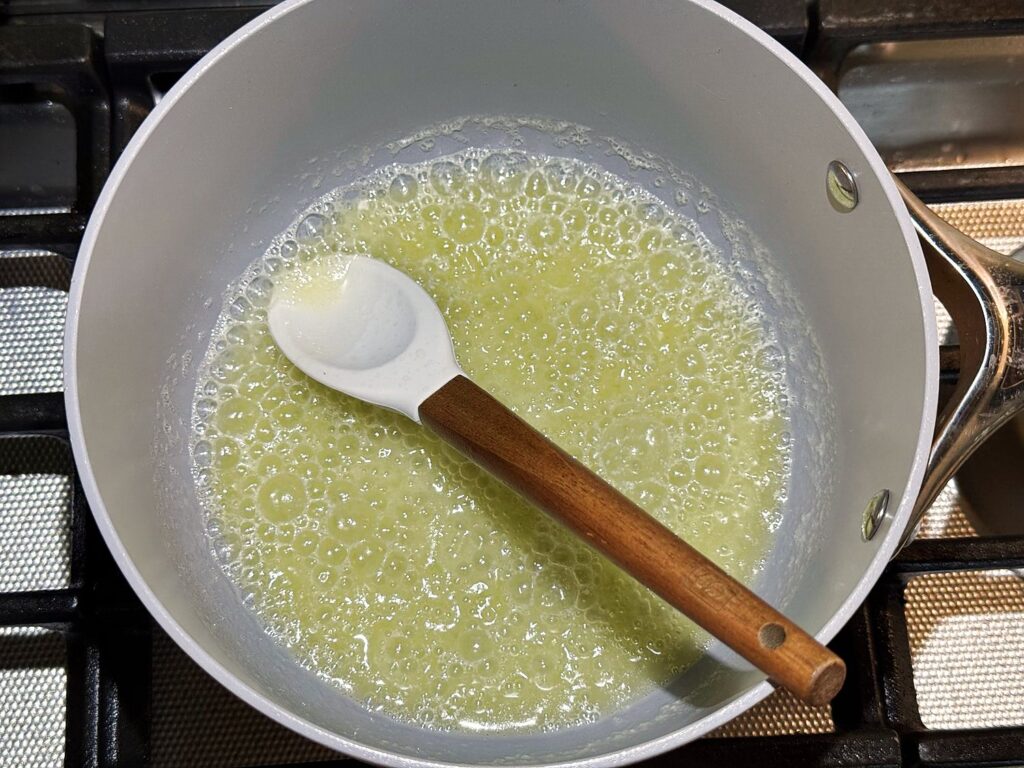 Melted butter foaming and bubbling in a light colored saucepan on a gas stove