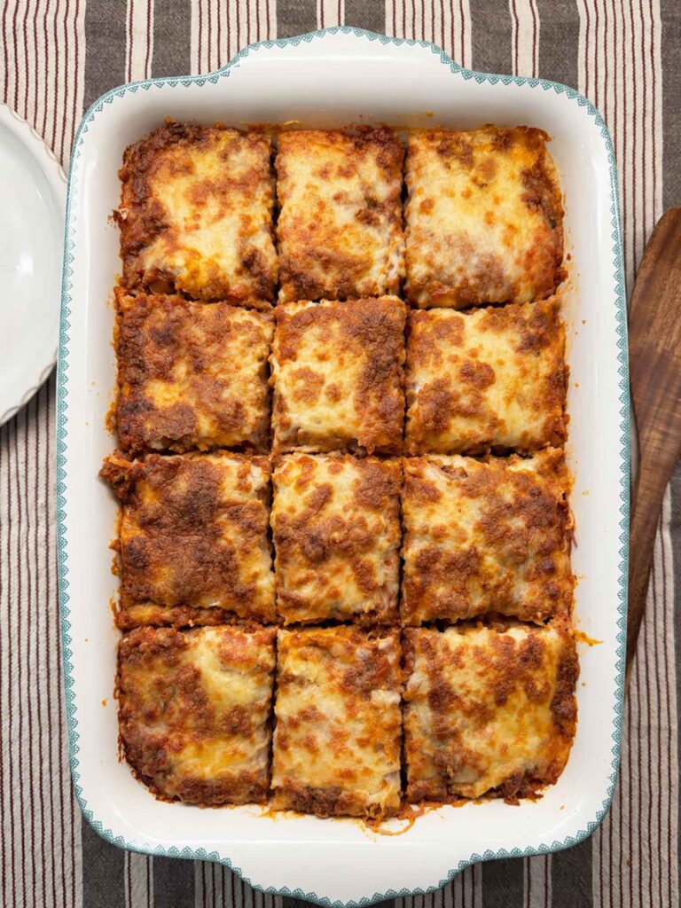 Baked million dollar spaghetti cut into 12 clean squares in the white 9x13 baking dish.