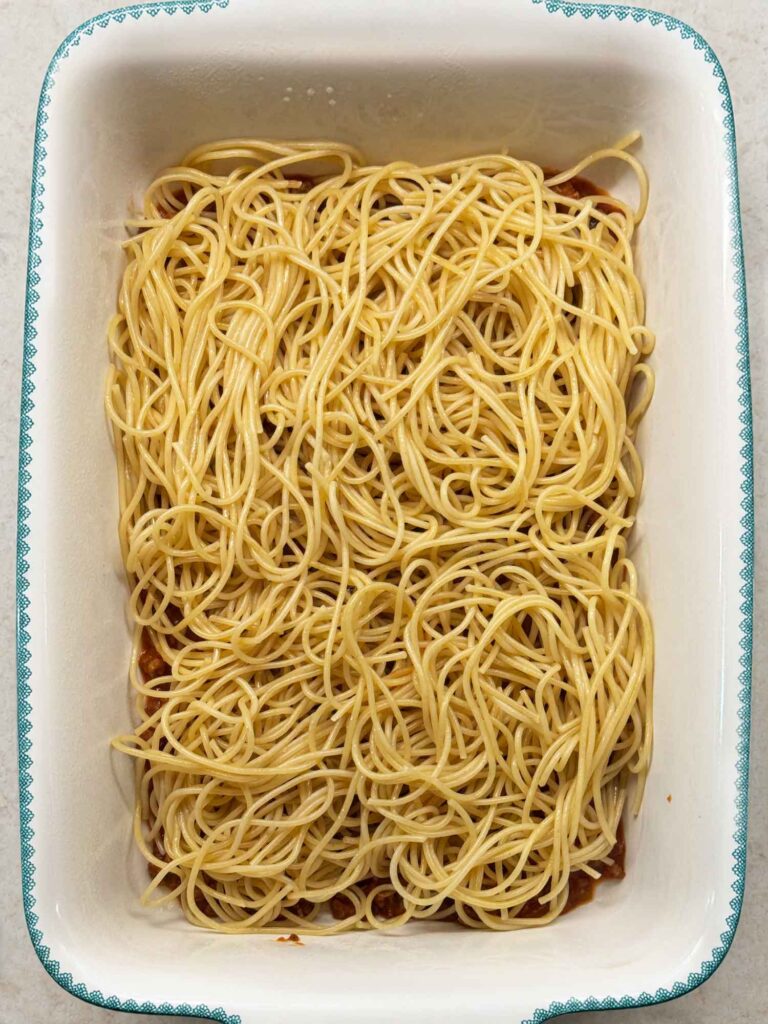 Buttered spaghetti spread in an even layer over the sauce in the baking dish.