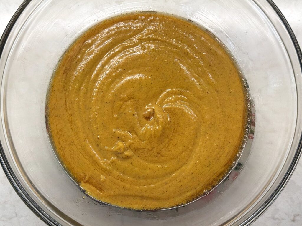 Thick golden pumpkin bread batter flecked with spices in a glass bowl
