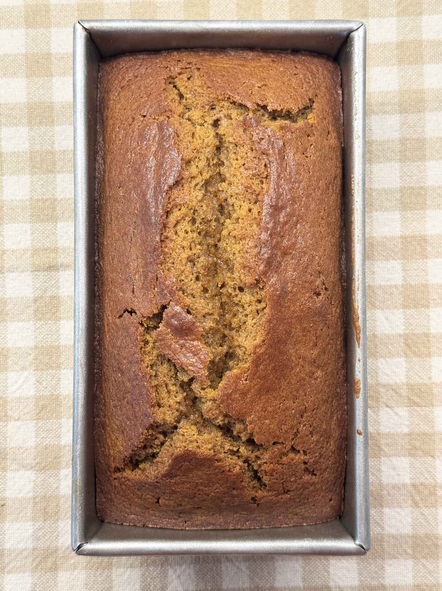 Baked pumpkin bread in its loaf pan with a split running down the center of the domed top