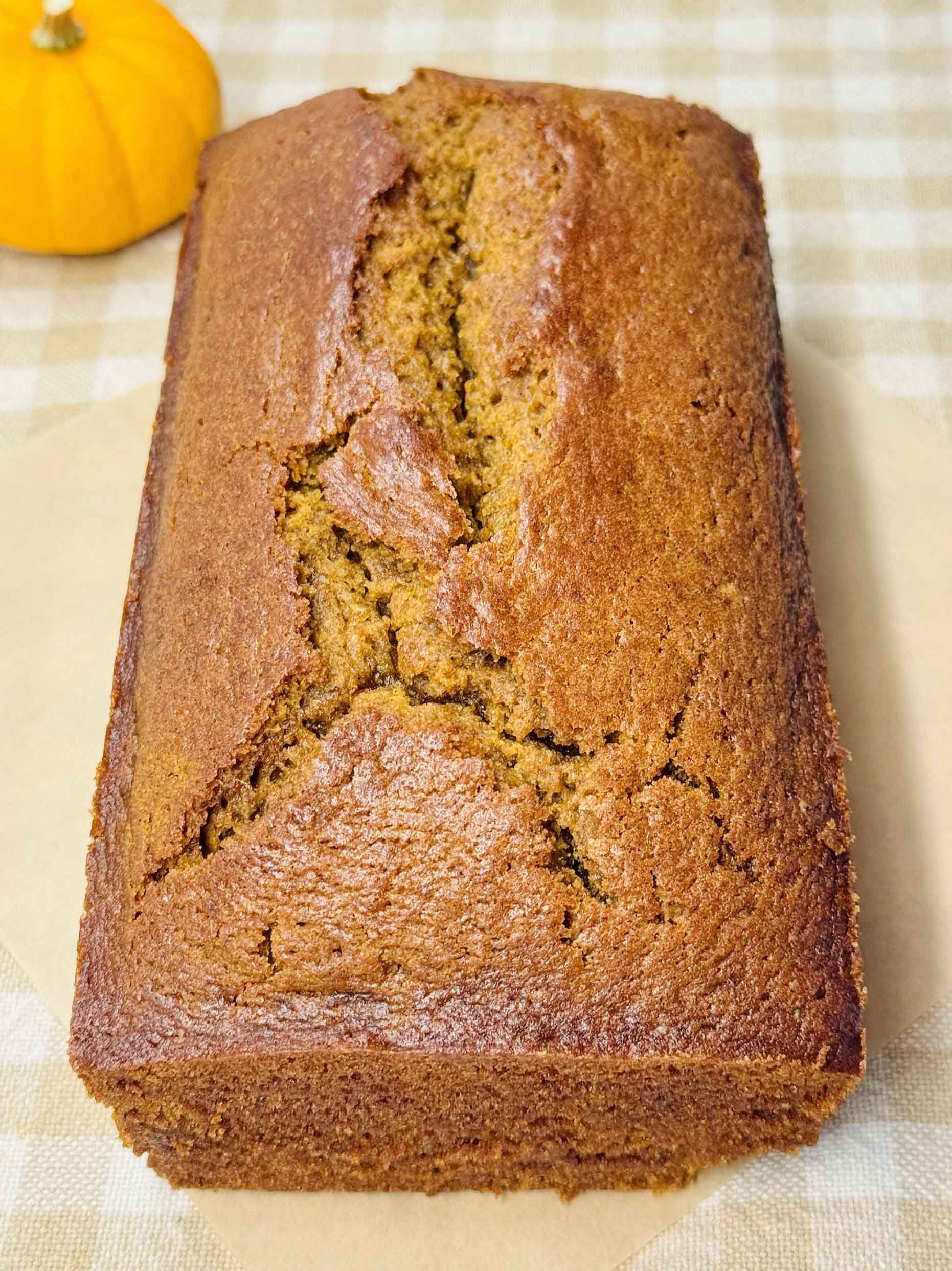 Whole loaf of pumpkin bread cooled on parchment with a small orange pumpkin beside it