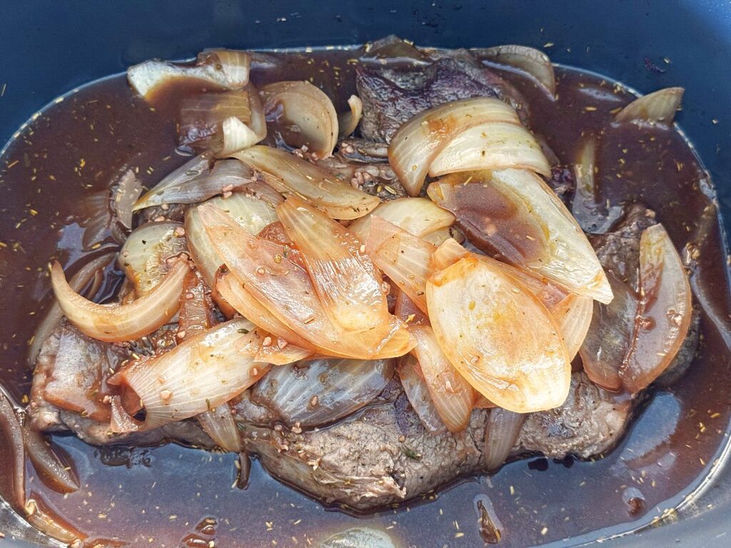 Seared chuck roast in the slow cooker with the wine and onion braising liquid poured over it