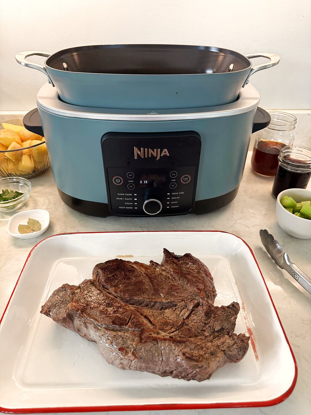 Seared chuck roast resting on a platter next to the multi cooker used to sear it