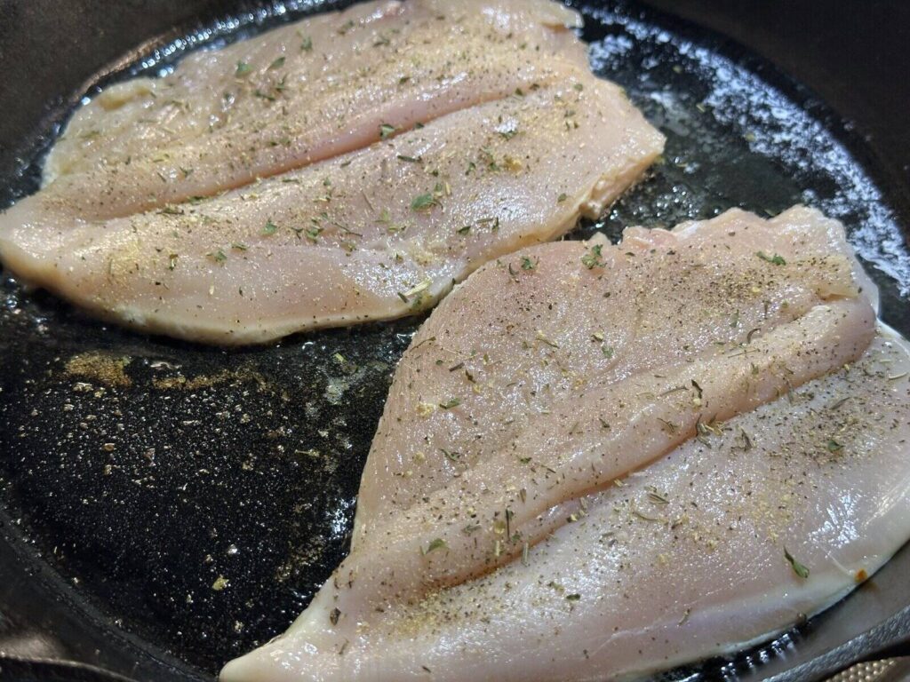 Seasoned chicken breasts searing in a cast iron skillet