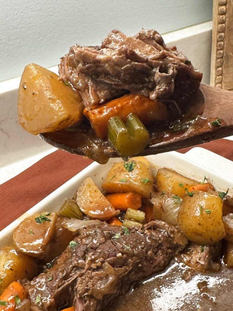 Serving slow cooker pot roast with a wooden spoon, tender beef with potatoes carrots and celery