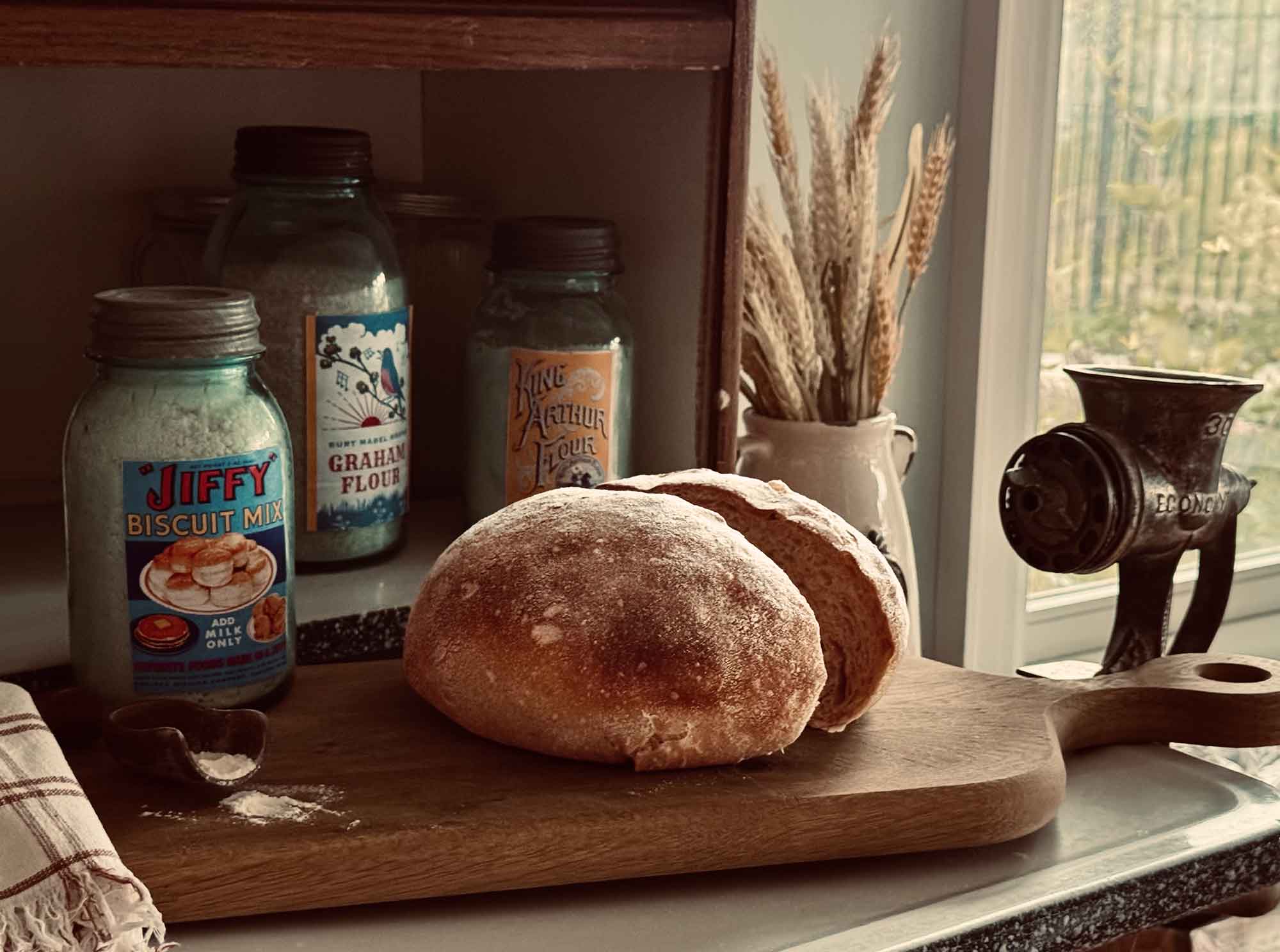 Still life photograph of sourdough bread on an antique Hoosier cabinet with vintage flour jars.