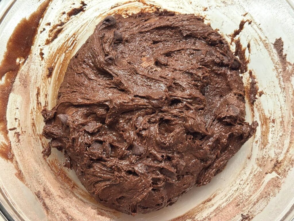 Very thick brownie batter with chocolate chips folded in, in a glass bowl