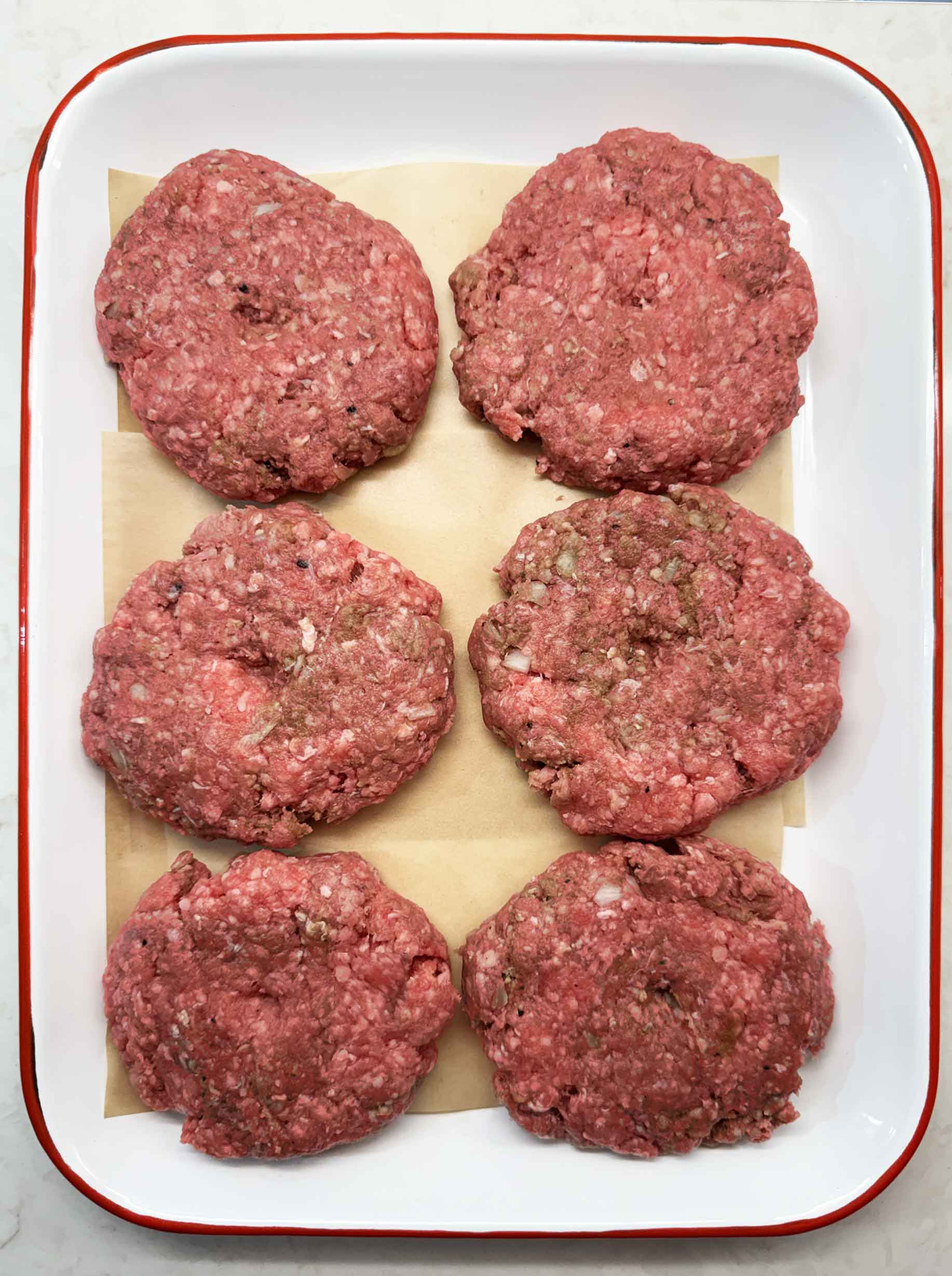 Formed raw burger patties on a parchment lined tray ready to chill