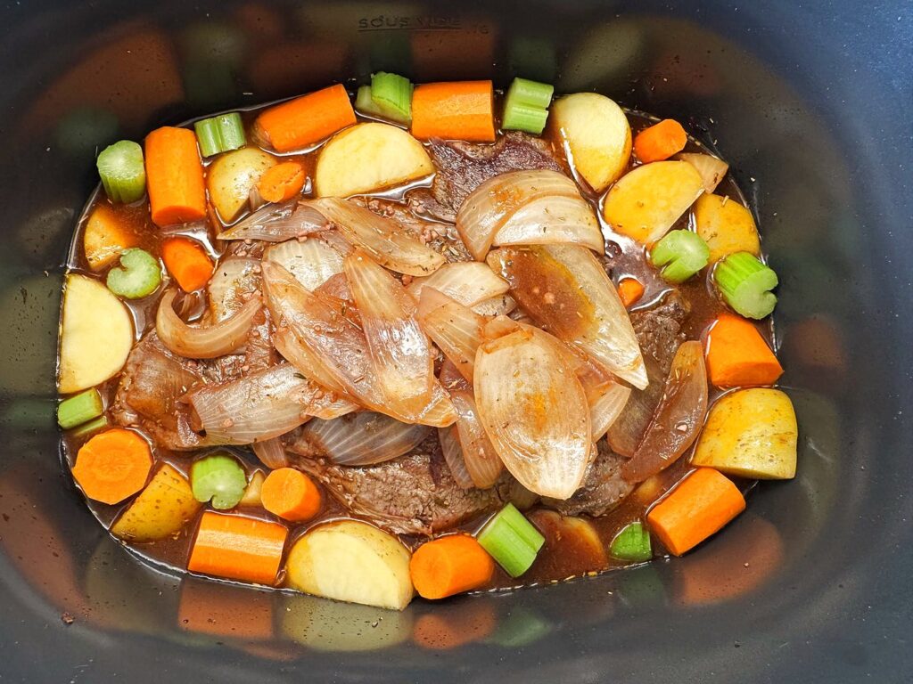 Potatoes, carrots, and celery arranged around the seared roast in the slow cooker before cooking