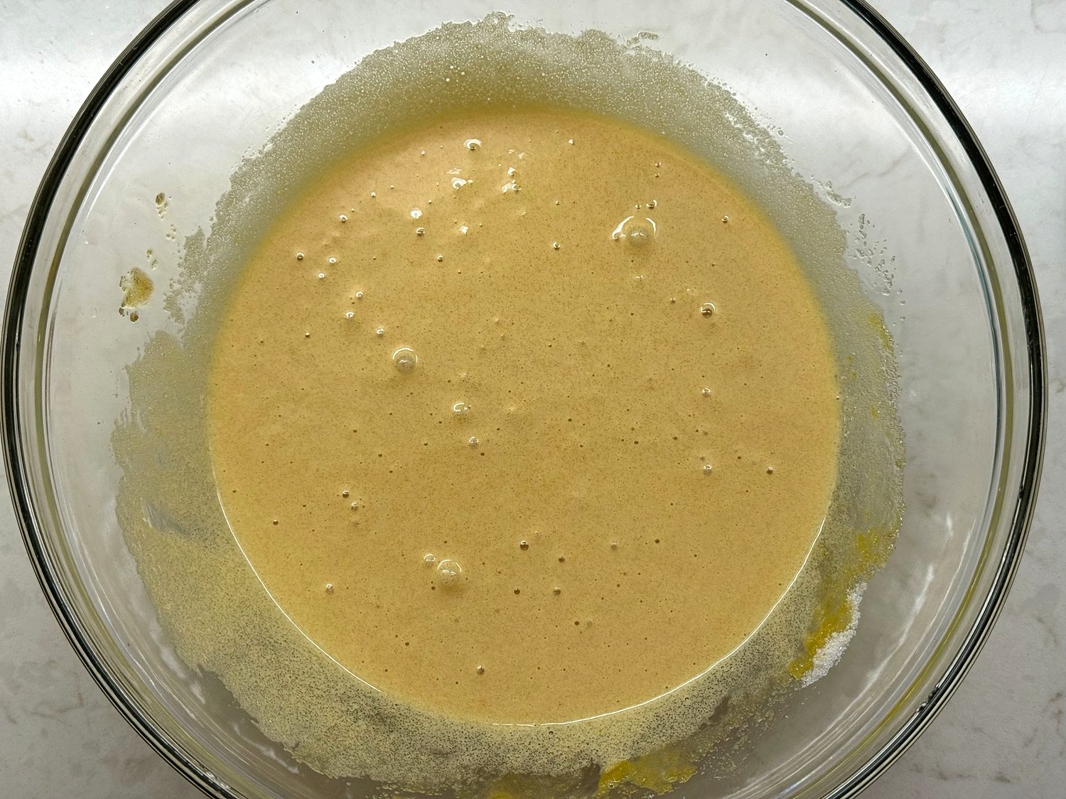 Pale, foamy egg and sugar mixture in a glass bowl after one minute of whisking