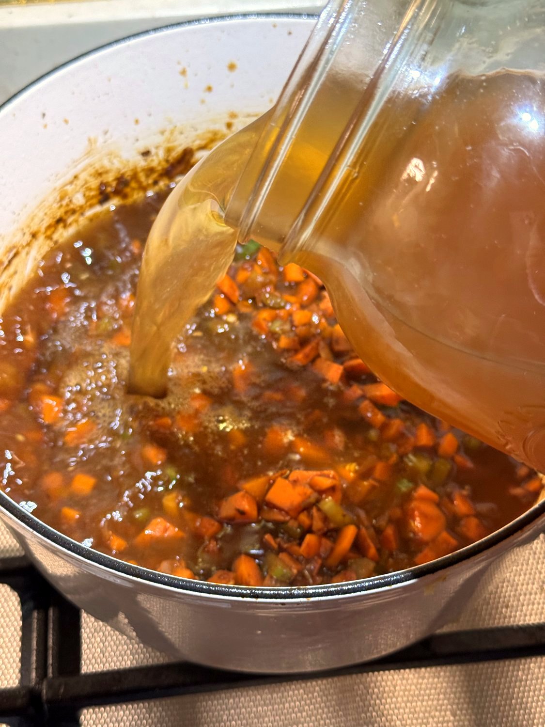 Beef broth being poured from a large jar into the soup pot