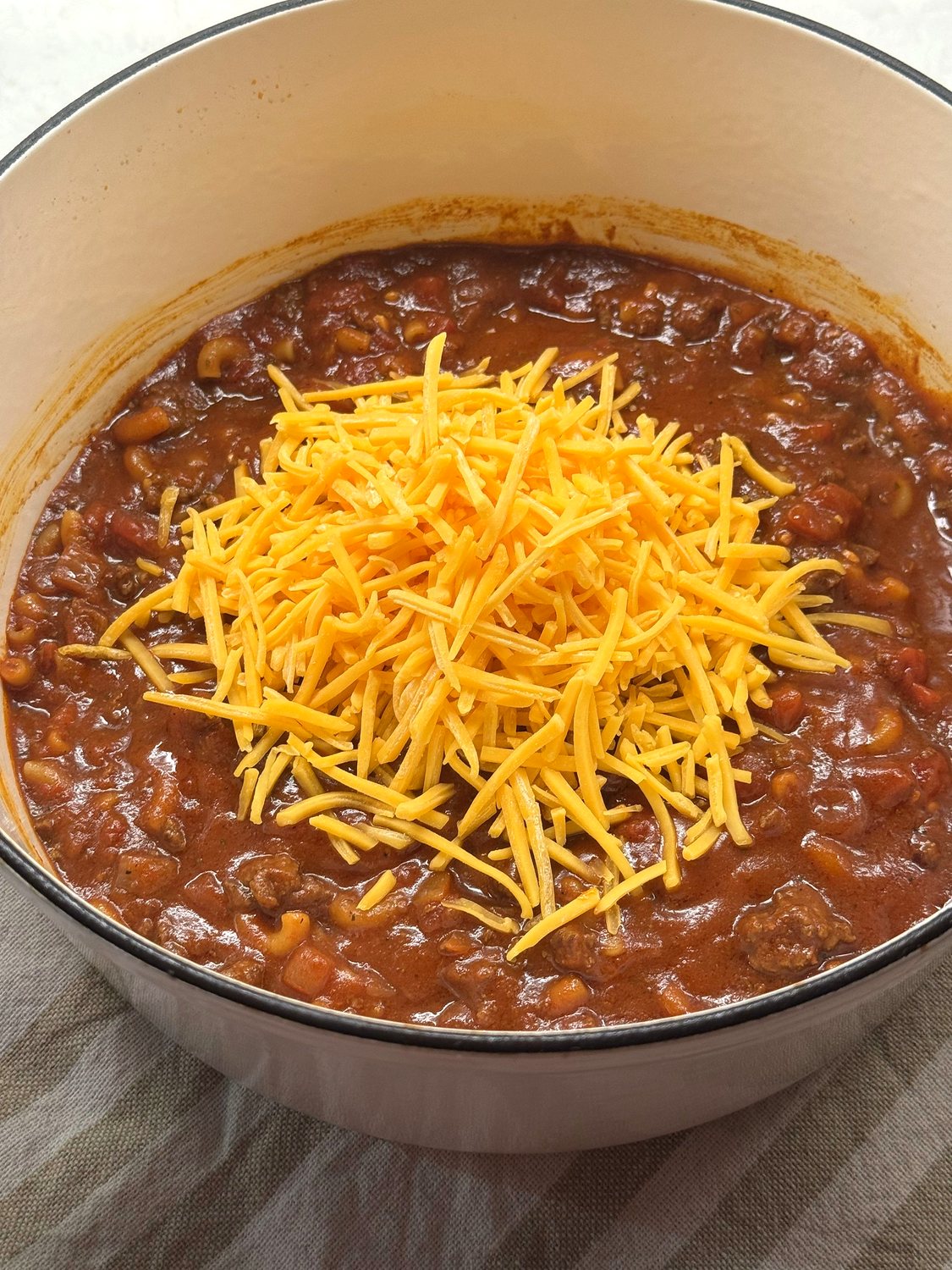Shredded sharp cheddar piled on top of venison goulash in a white Dutch oven