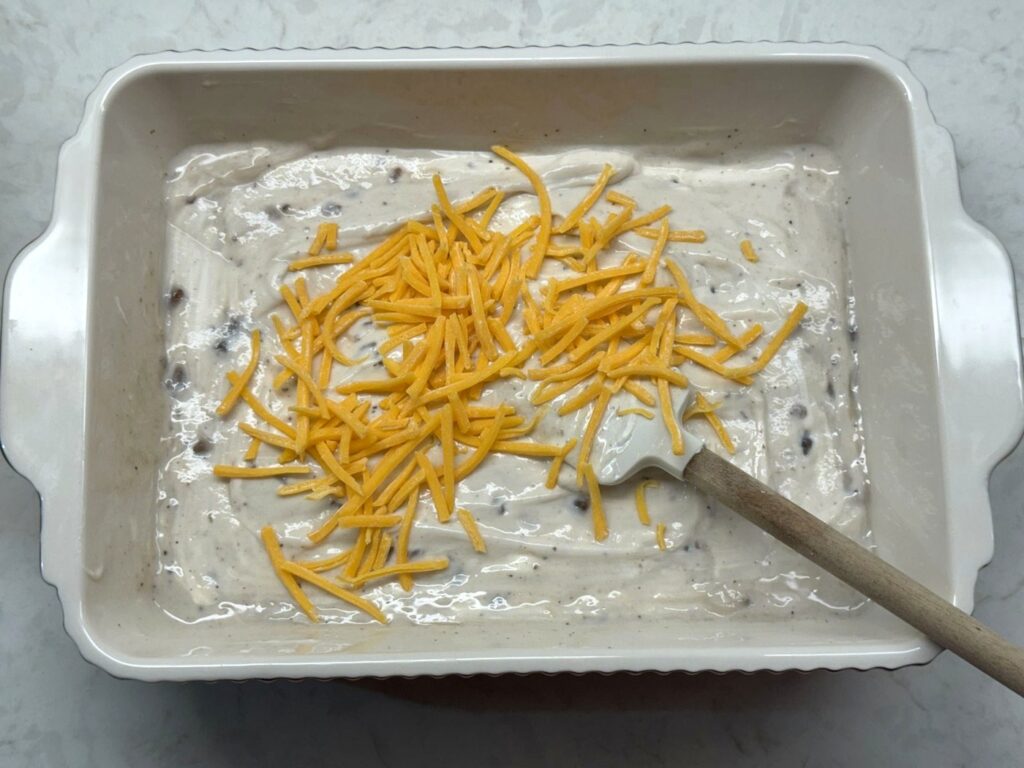 Shredded cheddar on top of the creamy sauce in the baking dish