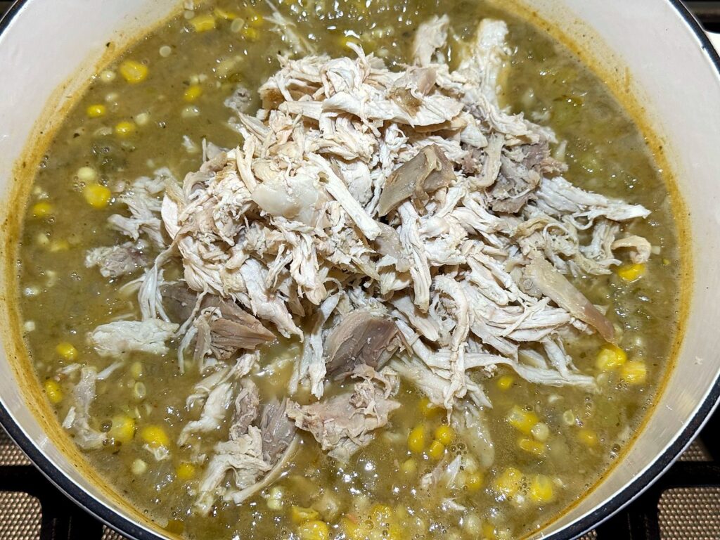 Shredded chicken piled on top of the chili with corn kernels in the Dutch oven
